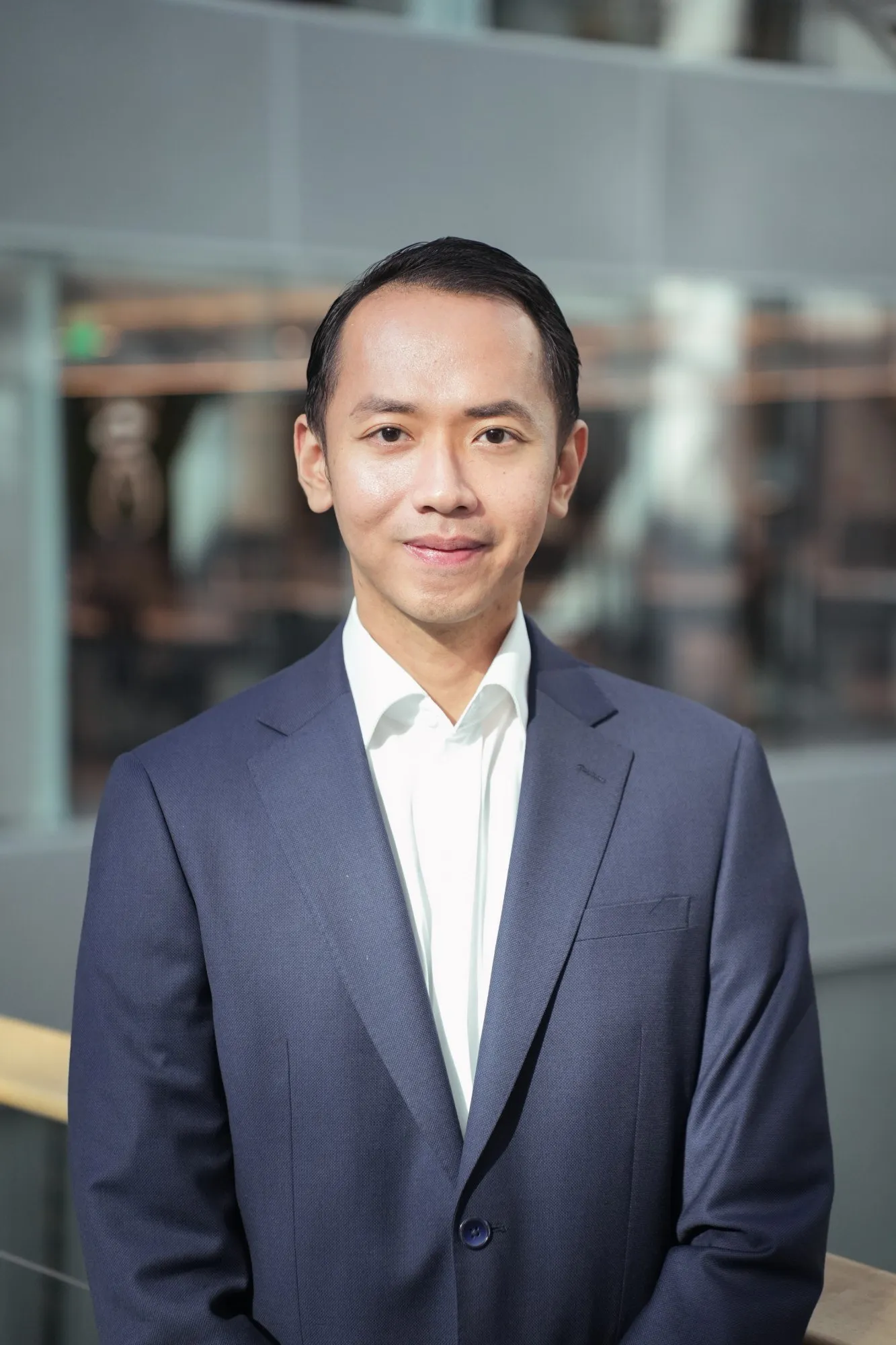 A professional portrait photo of Adrian Bex, smiling, in an office atrium.