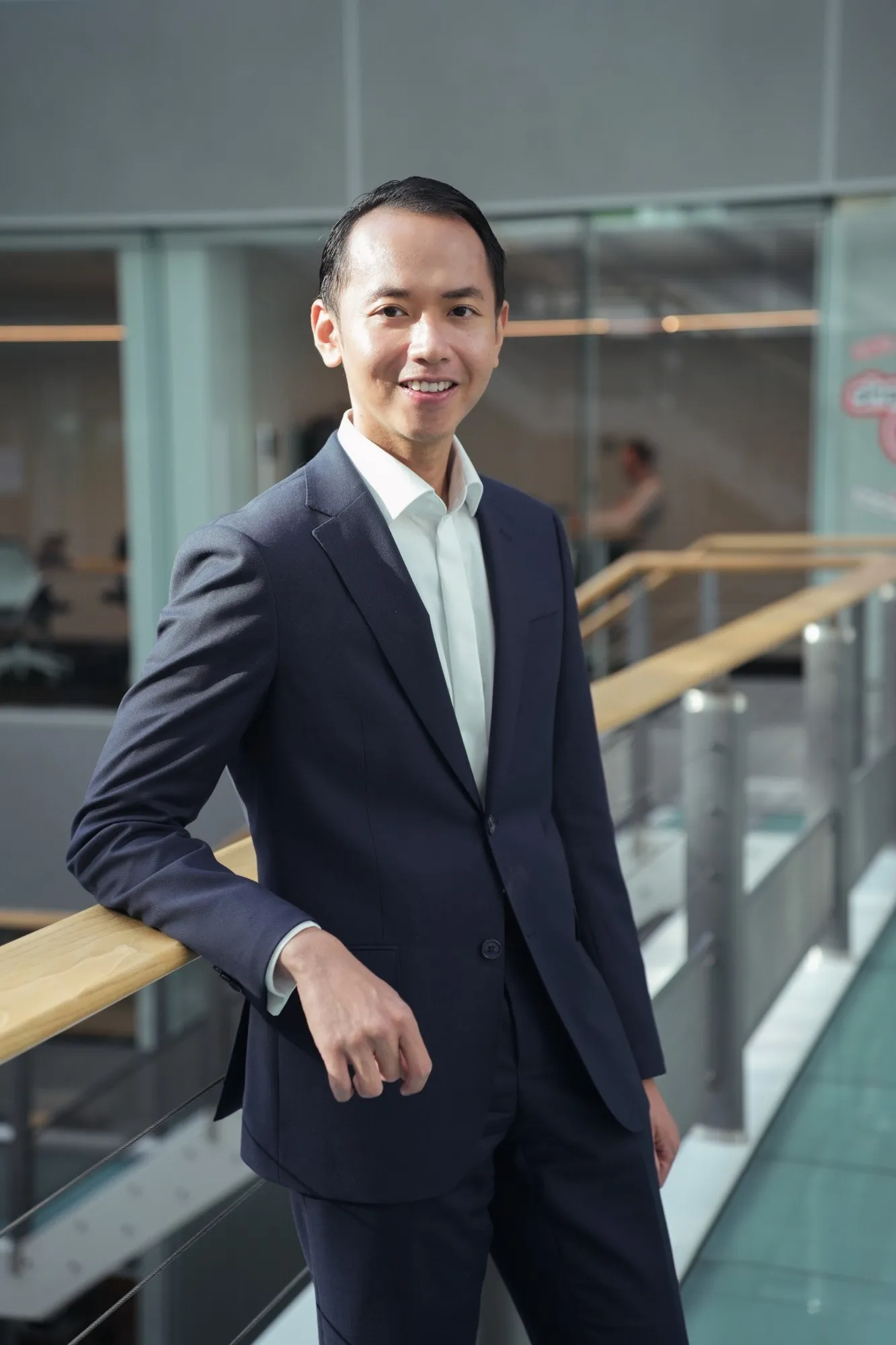 A professional portrait photo of Adrian Bex, leaning on a railing in an office atrium.